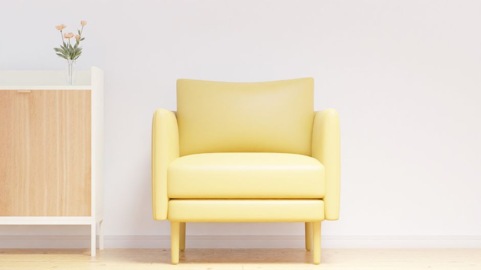 A stylish yellow armchair in a modern minimalist interior with wooden cabinet and flower vase.