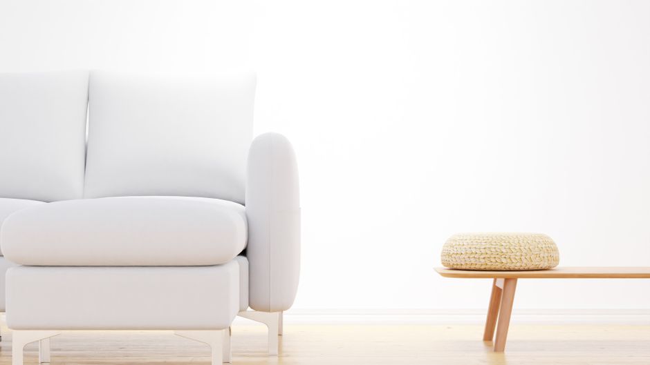 A serene minimalist living room featuring a white sofa and a wooden bench with a woven cushion, perfect for modern interiors.