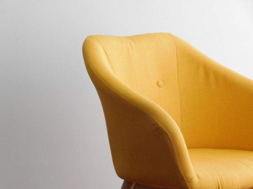 A bright yellow armchair stands against a white minimalist wall, showcasing modern design elegance.